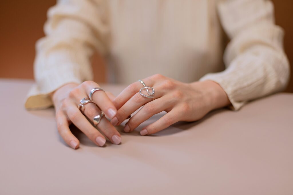 Close-up of hands adorned with stylish silver rings, showcasing modern jewelry design on a subtle background.